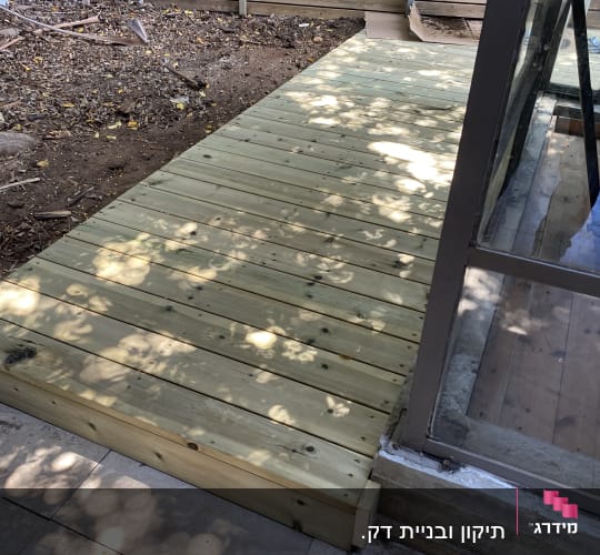 דק עץ חדש ליד חלון זכוכית בגינה